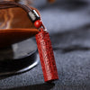 Close-up of a red cinnabar cylinder pendant with carved mantras on a brown cord.