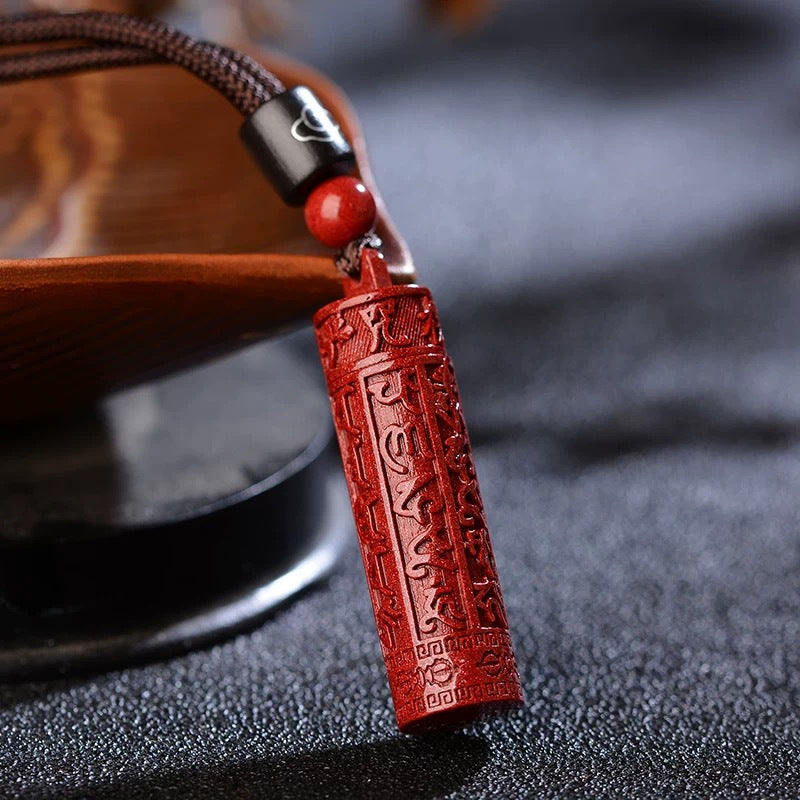 Close-up of a red cinnabar cylinder pendant with carved mantras on a brown cord.