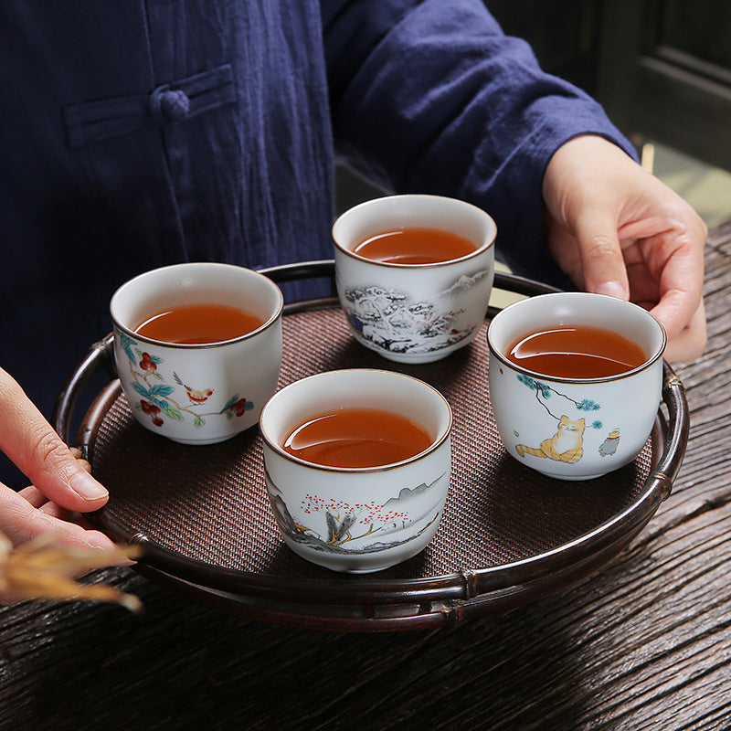 Four small white ceramic teacups with painted designs sitting on a round wooden tray