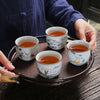 Four small white ceramic teacups with painted designs sitting on a round wooden tray