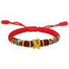 A close-up view of the red cord bracelet with a gold King Kong knot on a wrist