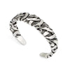 Silver-tone metal cuff bracelet with a twisted line texture worn on a man's wrist