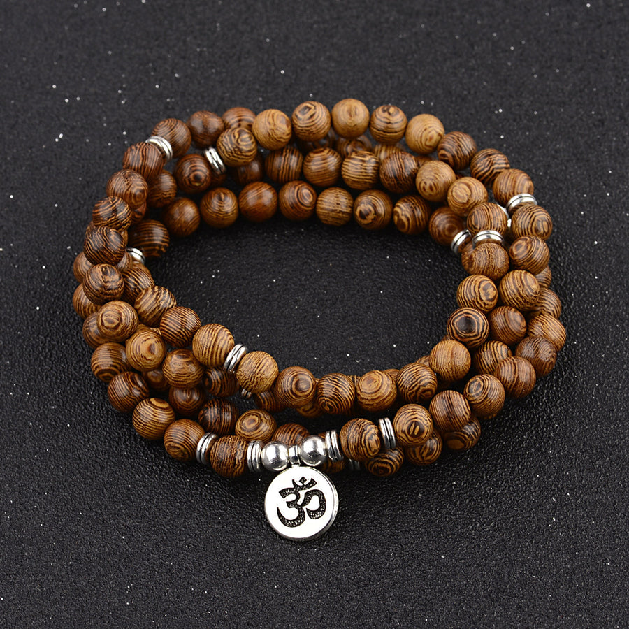 Coiled wooden bead mala bracelet with silver spacers and an Om charm on a dark background.