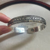 Close up of an antique silver cuff bracelet with Tibetan script and a lotus flower design