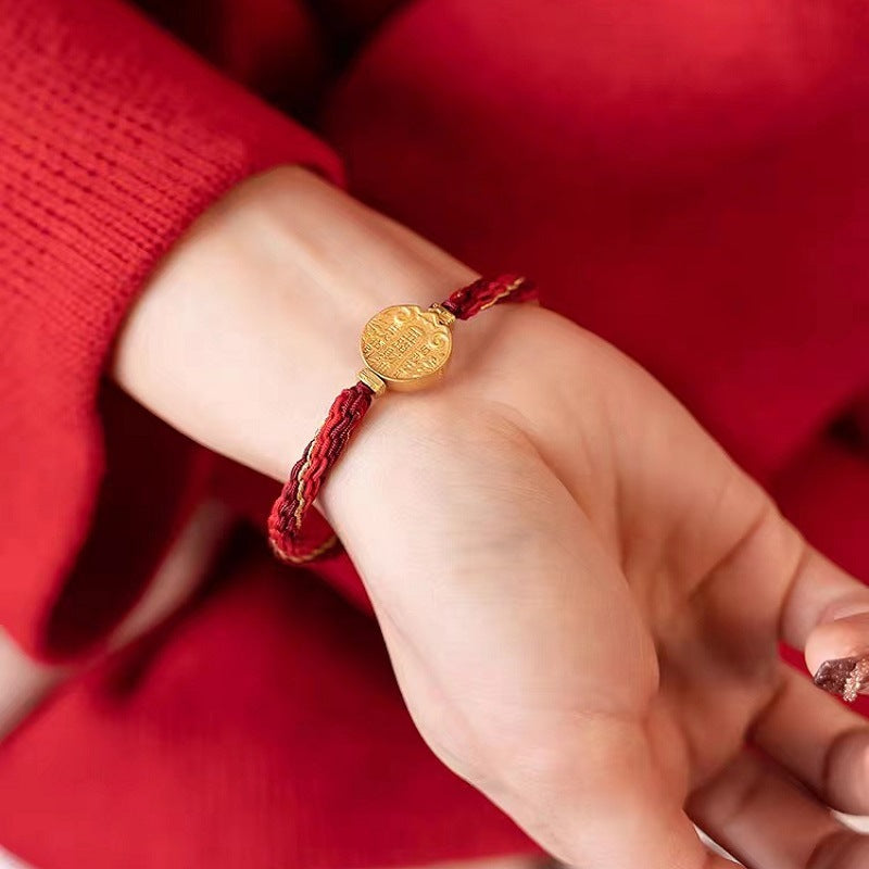 Gold-tone charm on a braided red string bracelet worn on a wrist