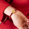 Gold-tone charm on a braided red string bracelet worn on a wrist