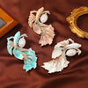 Three enamel fish brooches with faux pearls on a brown fabric background