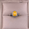 Close up of a vintage style sterling silver ring with a yellow oval stone on a cushion.
