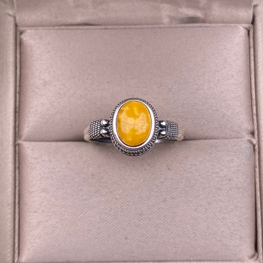 Close up of a vintage style sterling silver ring with a yellow oval stone on a cushion.