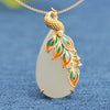 Close up of a white teardrop pendant with a gold tone phoenix and colorful enamel details on a blue background
