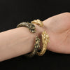 Two brass dragon bracelets worn on a wrist, one antique finish and one gold tone.