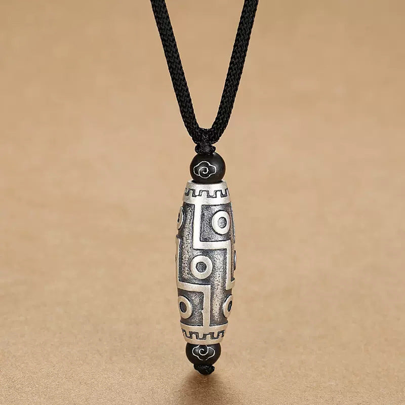 Close-up view of a copper nine-eye dzi bead pendant on a black cord against a tan background