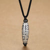 Close-up view of a copper nine-eye dzi bead pendant on a black cord against a tan background