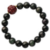 Close-up of a black obsidian bracelet with a red carved cinnabar bead on a wooden surface