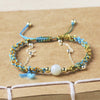Close up of a handmade blue and gold-tone woven bracelet with a white jade bead