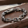 Close up of an engraved copper chain bracelet with a barrel clasp resting on a brown leather surface