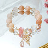 Close up of a pastel pink beaded bracelet with a gold flower charm