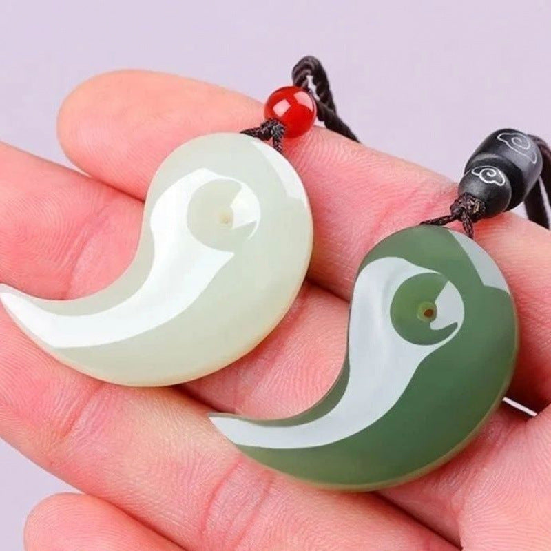 Hand holding a pair of white and green jade pendants shaped like yin yang curves