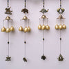 Four gold-tone metal wind chimes hanging against a white wall