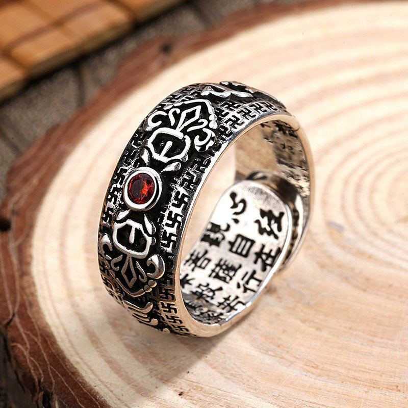 Close up of an adjustable copper ring with carved patterns and a red stone