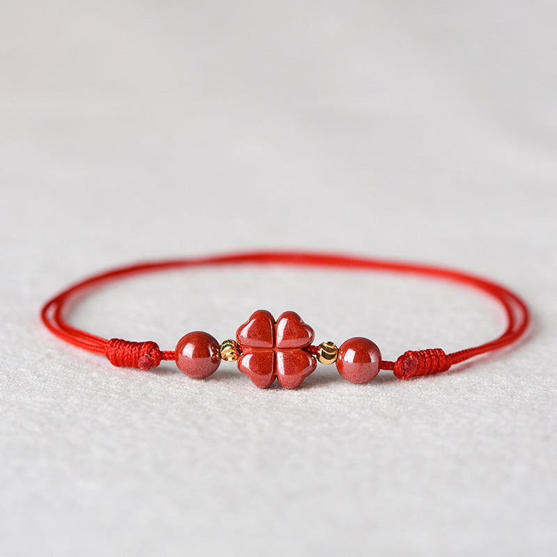 Red string bracelet with a central cinnabar four-leaf clover charm and round beads