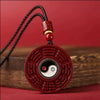 Close up of a round red cinnabar pendant with Bagua trigrams and a spinning Yin Yang center on a black cord
