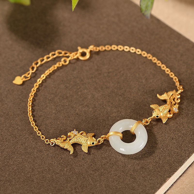 Gold-tone bracelet with white jade ring and two koi fish charms resting on a book