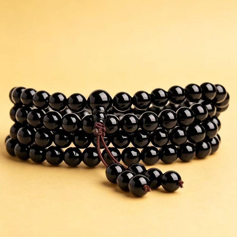Coiled 108 bead mala bracelet made of black and gold sheen obsidian stones on a yellow background