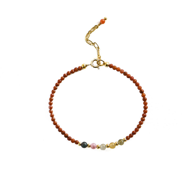 Close up of a thin red beaded bracelet with small accent beads and a gold clasp on a white background