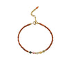 Close up of a thin red beaded bracelet with small accent beads and a gold clasp on a white background