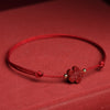 Close up of a red string bracelet with a small cinnabar flower charm on a wrist