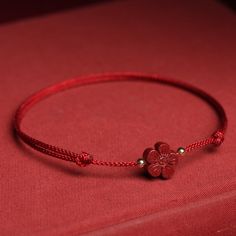 Close up of a red string bracelet with a small cinnabar flower charm on a wrist