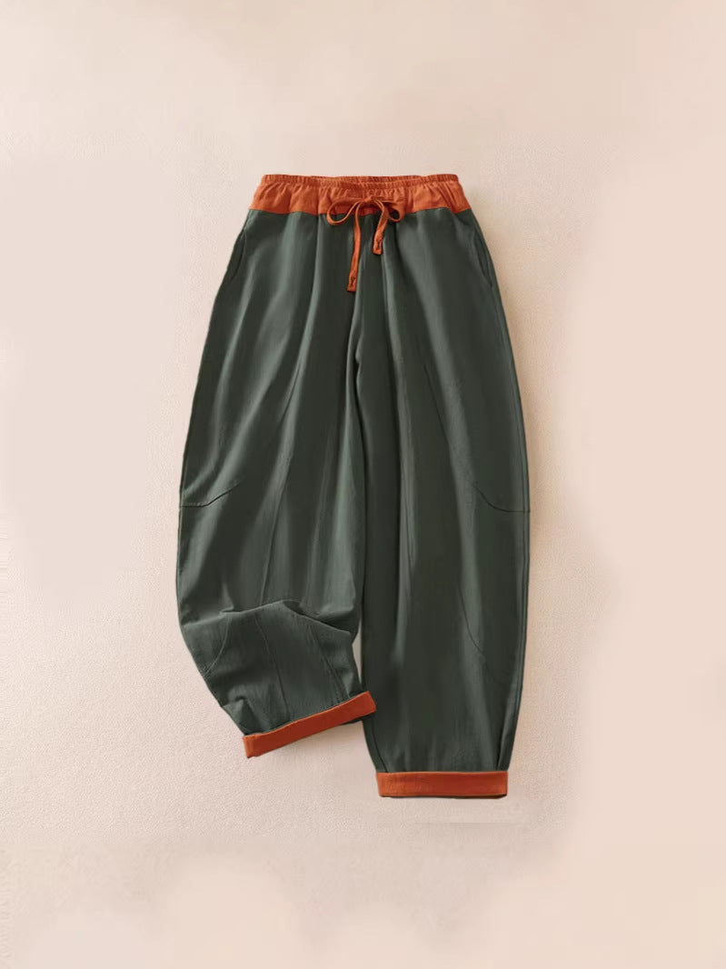 Olive green cotton harem pants with rust-colored waistband and cuffs laid flat on beige background