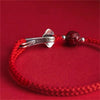 Close up of a red woven bracelet with a silver ruyi charm and a dark red bead
