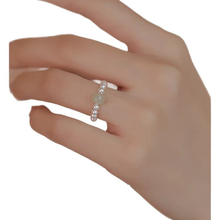 Close up of a hand wearing an adjustable ring with white pearls and green stones