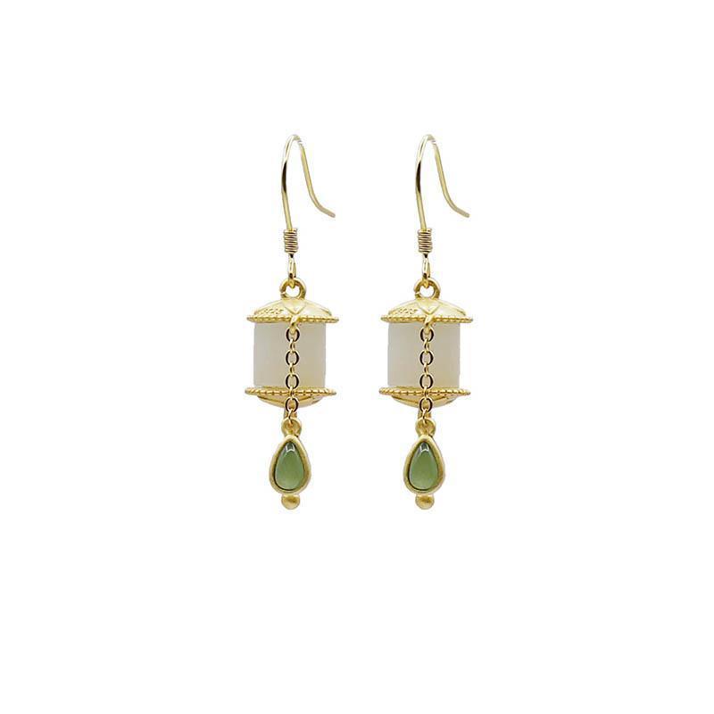 Gold-tone prayer wheel earrings with white jade cylinders and green drops hanging from a branch.