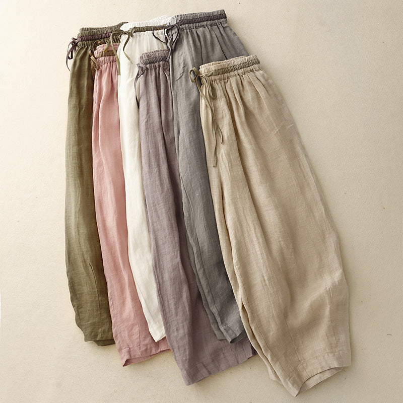 A flat lay of six pairs of loose linen harem pants in muted earth tones.