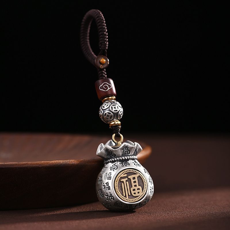 Hand holding a silver-tone metal money bag keychain with gold-tone Fu character details