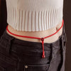 Model wearing a red woven cord waist chain with a hanging cinnabar bead over dark jeans