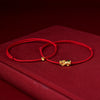 Close up of a red braided cord bracelet with a small gold pixiu charm
