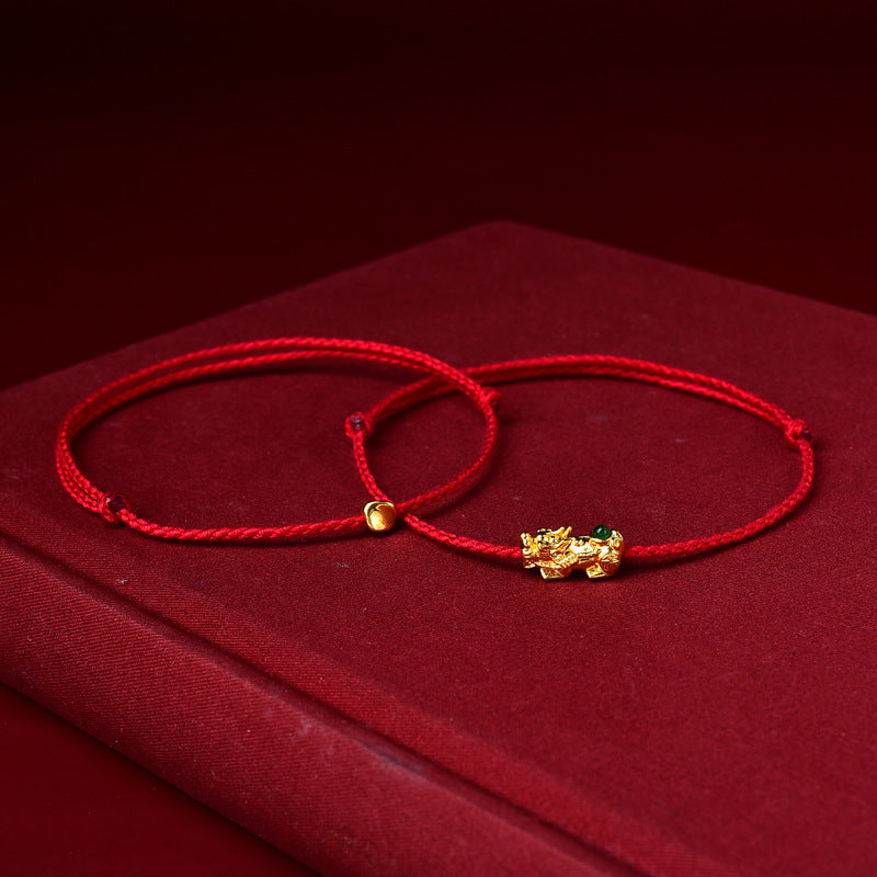 Close up of a red braided cord bracelet with a small gold pixiu charm
