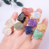 A hand wearing multiple natural crystal rings with gold-tone wire wrapping