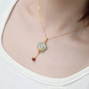 Gold necklace with a green jade plum blossom pendant and red bead accent worn on a model