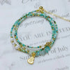 Triple wrap turquoise beaded bracelet with gold heart charm on white background