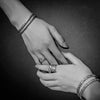 A black and white photo showing two hands wearing matching engraved rings and bracelets.
