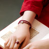 Close up of a wrist wearing a red braided bracelet with a small silver square charm
