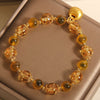 Close up of a yellow beaded bracelet with a gold lucky bag charm on a box