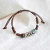Close up of a brown woven bracelet with silver tone metal and blue ceramic beads