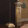 A tall gold-tone metal incense burner shaped like a pagoda with script etched into the sides
