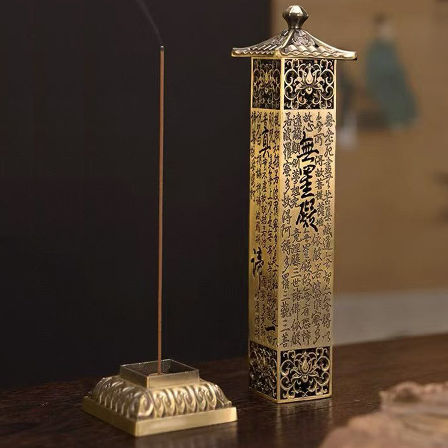 A tall gold-tone metal incense burner shaped like a pagoda with script etched into the sides